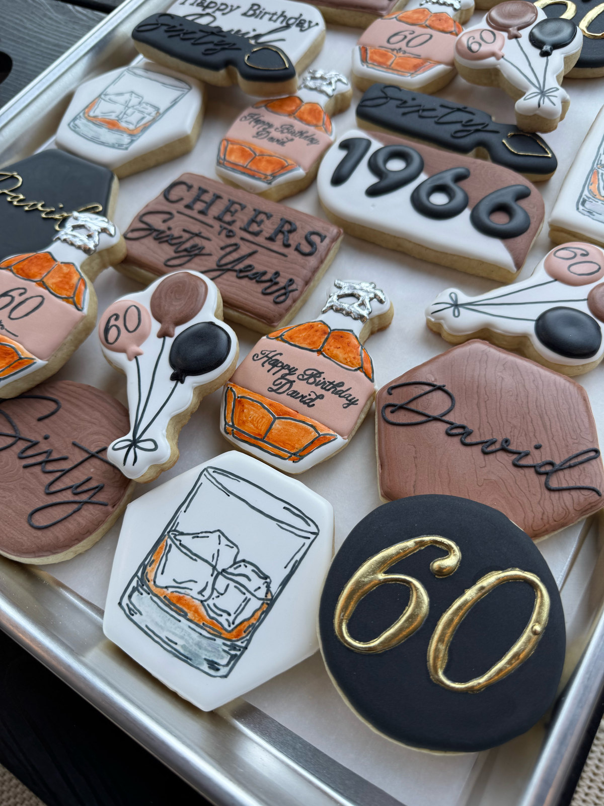 Hand-decorated 60th birthday cookies with gold 60s and a whiskey glass